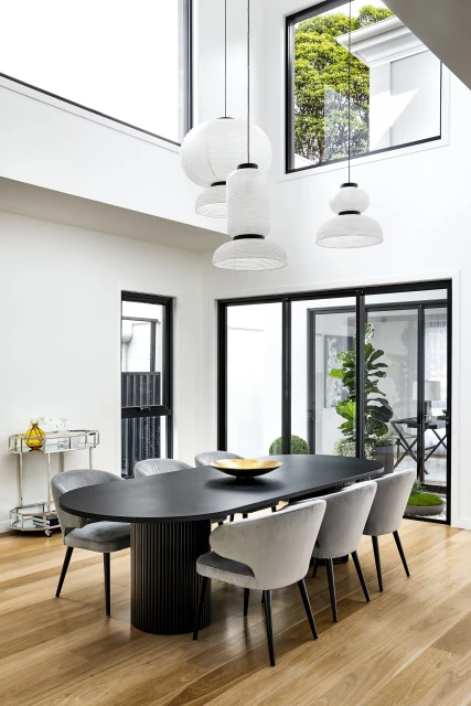Contemporary dining room featuring a black oval table surrounded by gray chairs under unique white pendant lights, light wood flooring.
