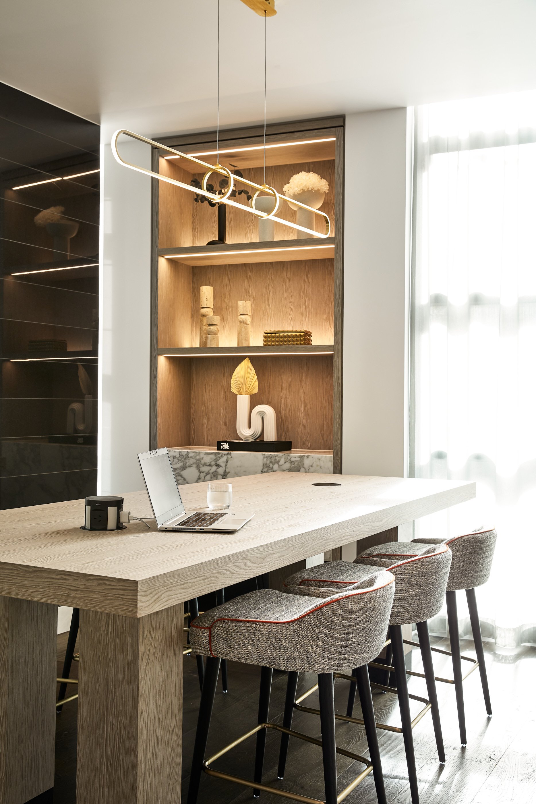 Modern interior showcasing a light wood table, bar stools, and a decorative shelf unit with ambient lighting and artistic objects.