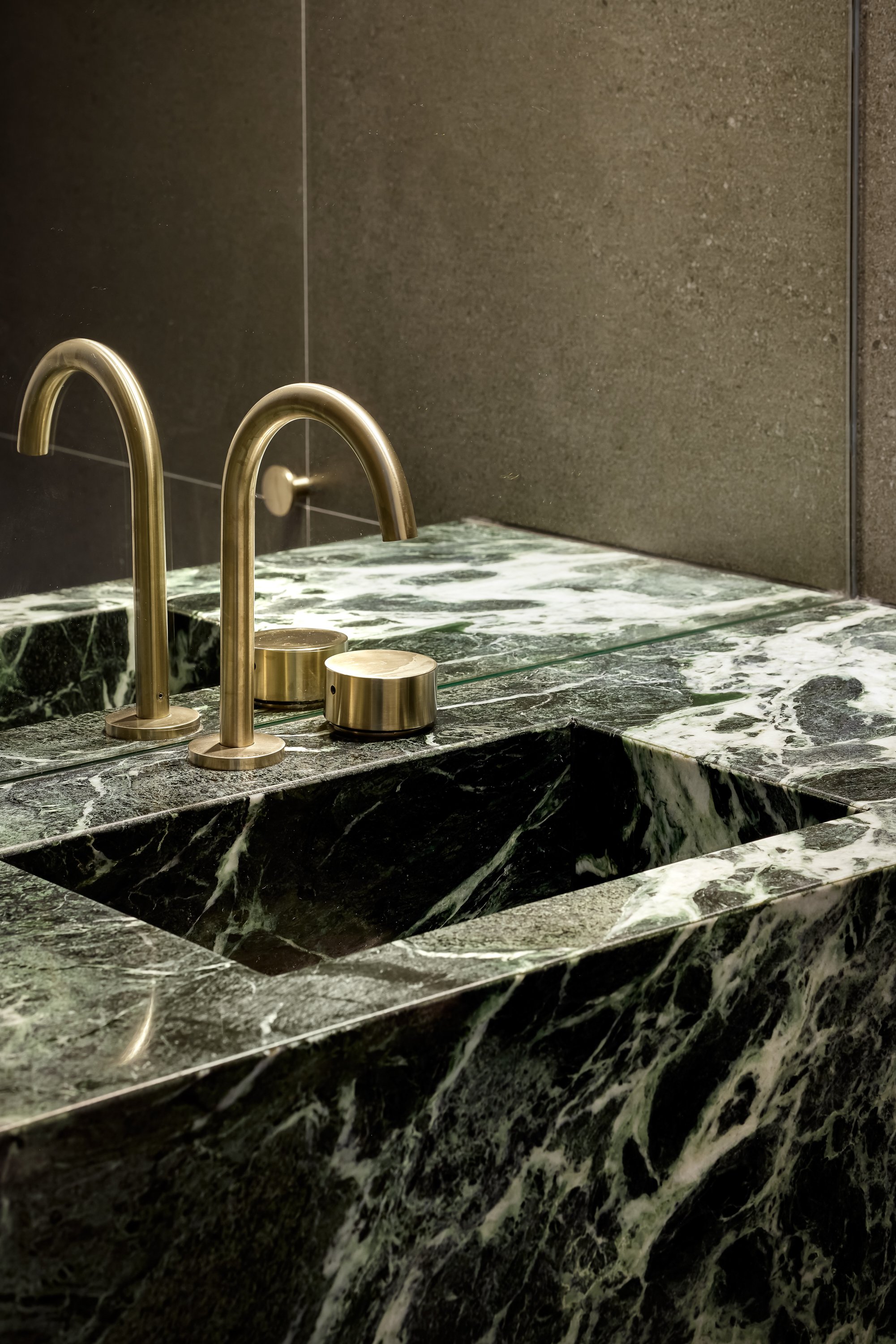Close-up of a green marble countertop featuring golden brass fixtures, including two curved faucets and cylindrical handles.