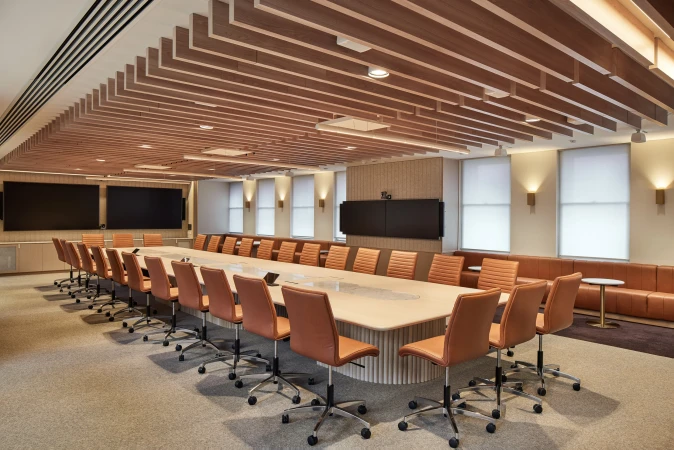 Bright, modern conference room features long table with tan leather chairs, light wood ceiling slats, and recessed and sconce lighting.