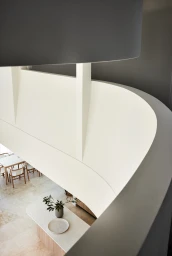 High angle interior view showing curved white architectural balcony wall overlooking kitchen and dining area in Sydney by Ryan Linnegar