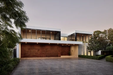 Modern architectural two-story house exterior with large glass panels, dark wood slats, and a wide driveway at dusk.