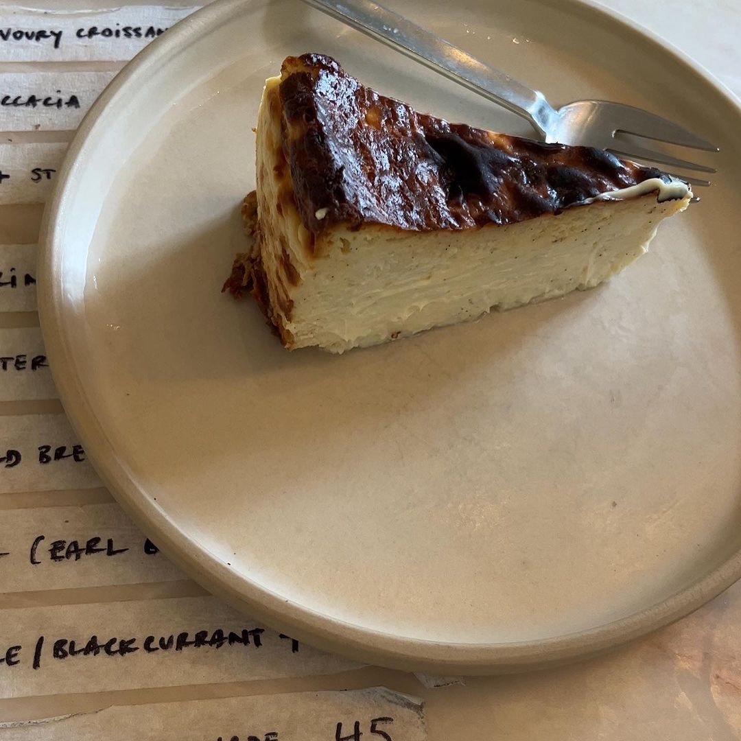 Slice of burnt Basque cheesecake with a fork on a beige plate sitting on a table with a printed menu, close-up food shot.
