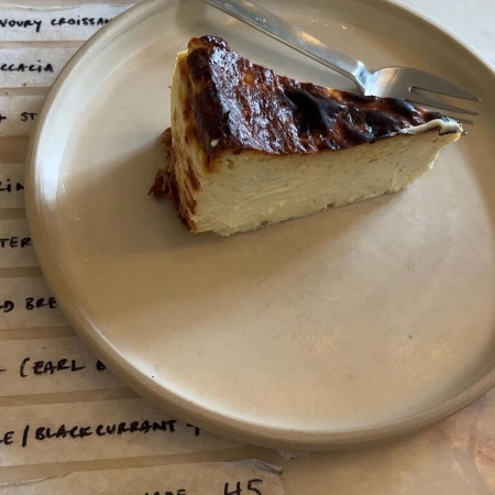 Slice of burnt Basque cheesecake with a fork on a beige plate sitting on a table with a printed menu, close-up food shot.