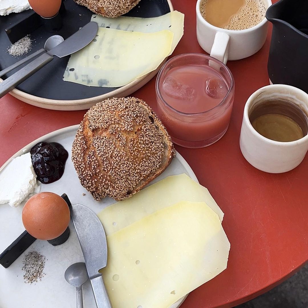 Overhead shot of a breakfast spread featuring bread, cheese, eggs, jam, and beverages on a red table. Food photography, still life.