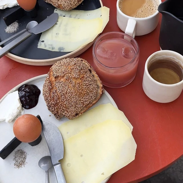 Overhead shot of a breakfast spread featuring bread, cheese, eggs, jam, and beverages on a red table. Food photography, still life.
