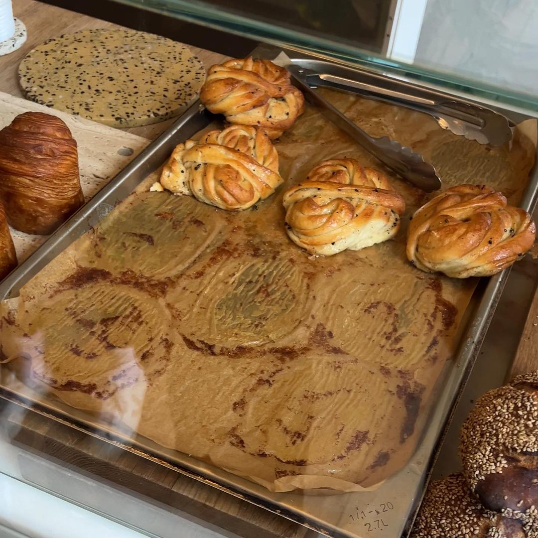Overhead shot of braided buns arranged on parchment paper on a baking sheet with a croissant and seeded bread in the background.
