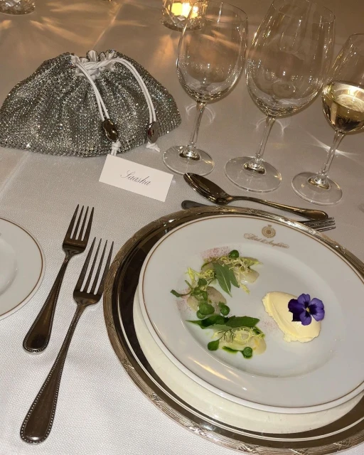 Elegant table setting featuring a plate with a colorful appetizer, fine silverware, crystal wine glasses, and a silver beaded purse.
