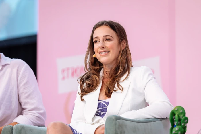 Content creator Samantha Gash wearing a white blazer seated on a panel in Sydney with a pink background