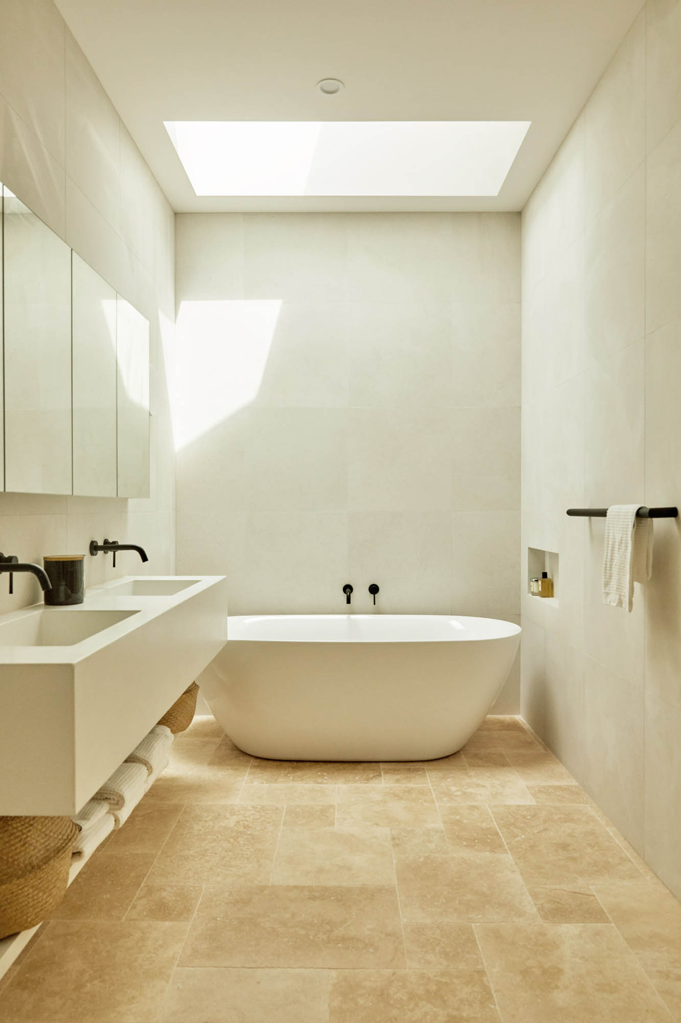 Bright bathroom interior featuring a white standalone tub, double sink vanity, and neutral tile flooring with a skylight overhead.