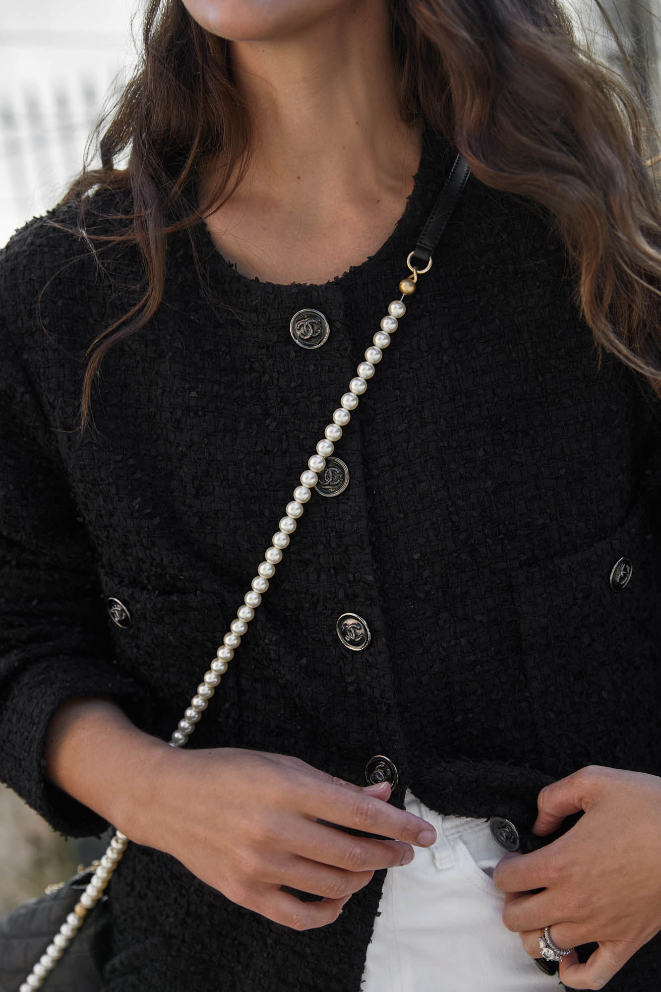 Black tweed jacket with decorative buttons and pearl strap, worn by an adult female. Shoulder shot.