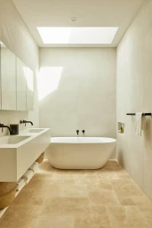 Modern minimalist bathroom featuring a freestanding white bathtub, double vessel sink vanity, and a large overhead skylight