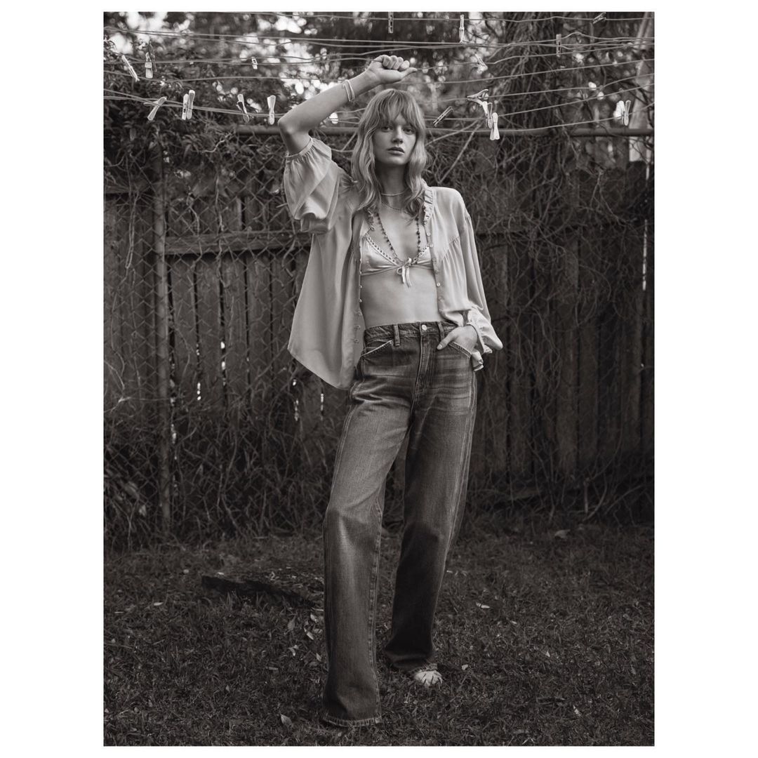 Monochrome portrait of a young fair-skinned woman in a relaxed pose outdoors wearing an unbuttoned blouse and denim jeans. Lifestyle fashion.
