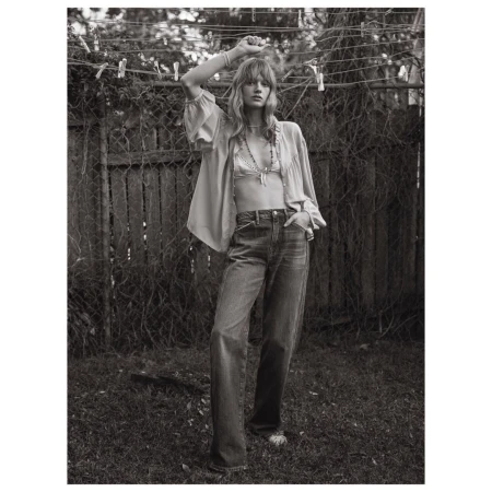 Monochrome portrait of a young fair-skinned woman in a relaxed pose outdoors wearing an unbuttoned blouse and denim jeans. Lifestyle fashion.
