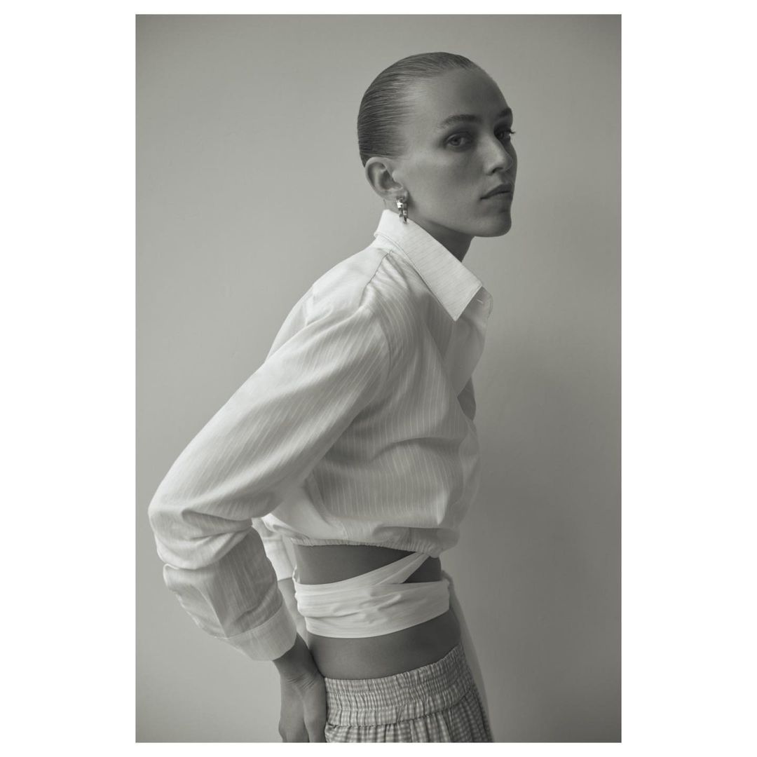 Portrait of a woman in a white crop top and patterned skirt against a neutral background in a studio with even lighting.