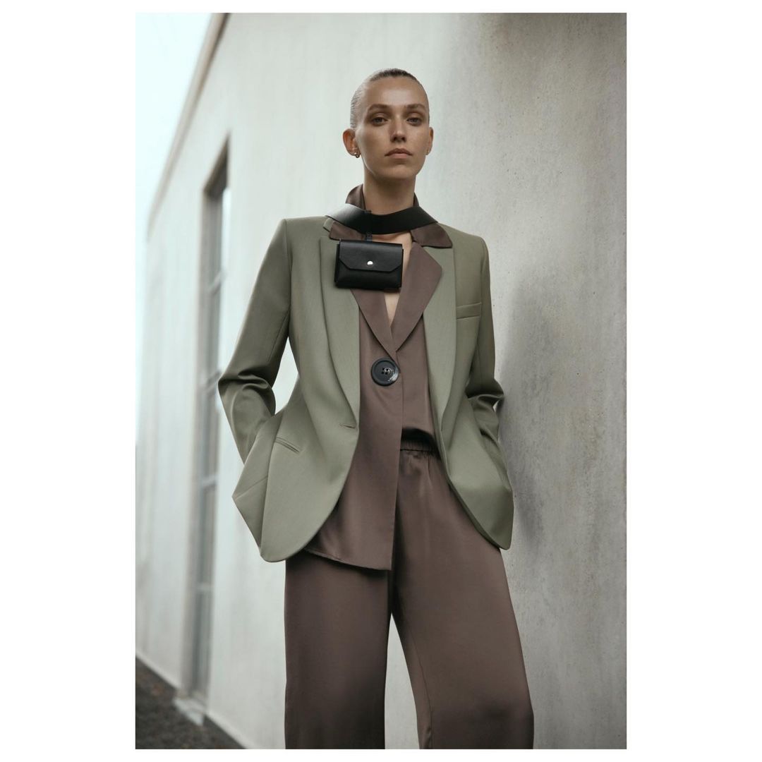 Stylish woman in a green blazer and brown pants poses against a modern building, showcasing a chic and fashionable ensemble.