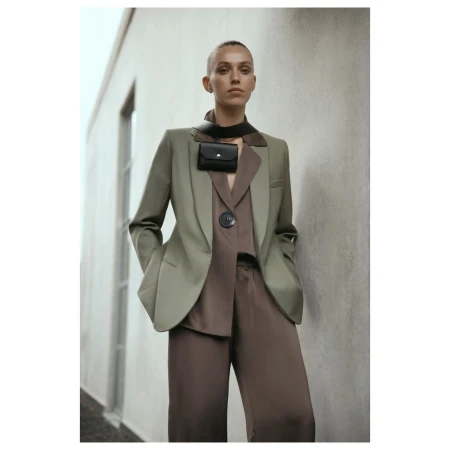 Stylish woman in a green blazer and brown pants poses against a modern building, showcasing a chic and fashionable ensemble.