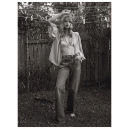 Monochrome fashion portrait of a female model in an unbuttoned blouse and jeans standing before a wire fence.