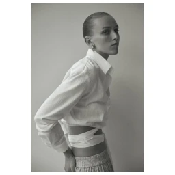 Monochrome portrait of a woman wearing a white collared wrap shirt and patterned trousers against a grey backdrop.