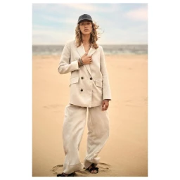 Model wearing a beige double breasted blazer and wide leg trousers standing on a sandy beach