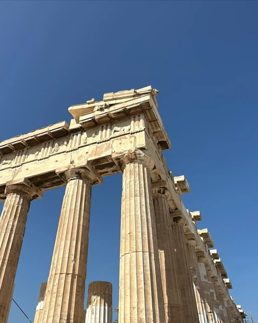 Low angle shot of the Parthenon in Athens, Greece, featuring its iconic columns and ancient architecture under a clear blue sky.