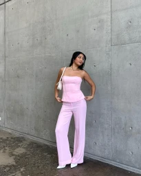 Woman in pink strapless top and pink trousers standing against a textured concrete wall