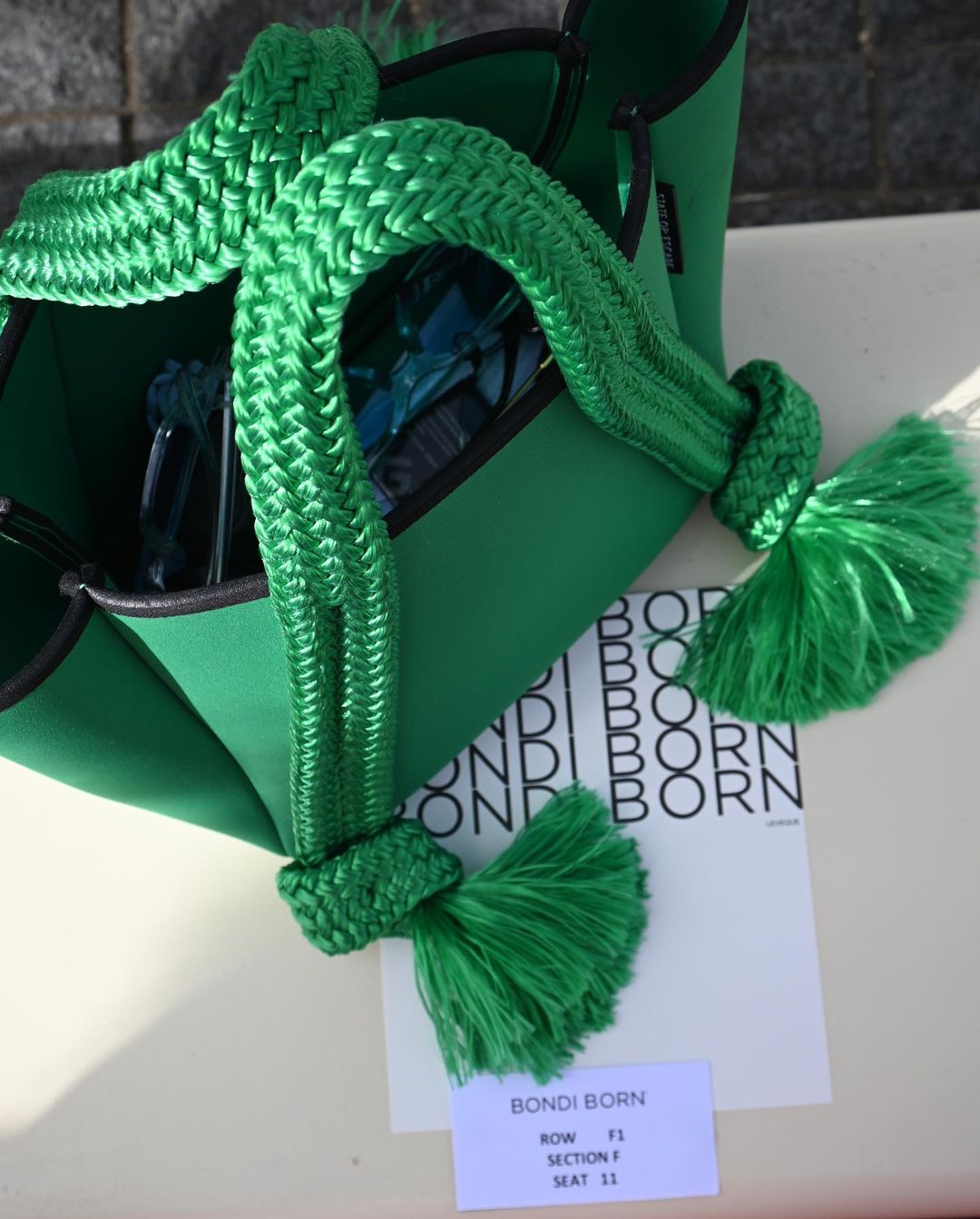 Lime green neoprene tote bag with braided rope handles and tassels, sitting on a white surface with a Bondi Born card nearby.