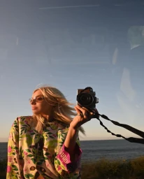 Blonde woman wearing floral patterned top holding vintage camera by the coast