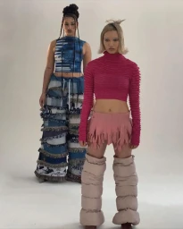 Two models posing against a white studio background wearing bright pink and blue patchwork clothing by Selina Yang.