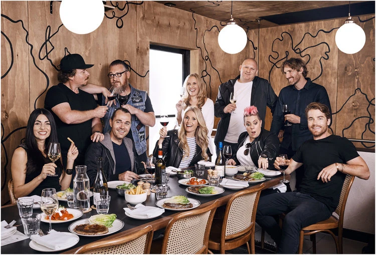 A group of ten people are seated around a table with wine glasses and plates of food in a warm and inviting indoor restaurant setting.
