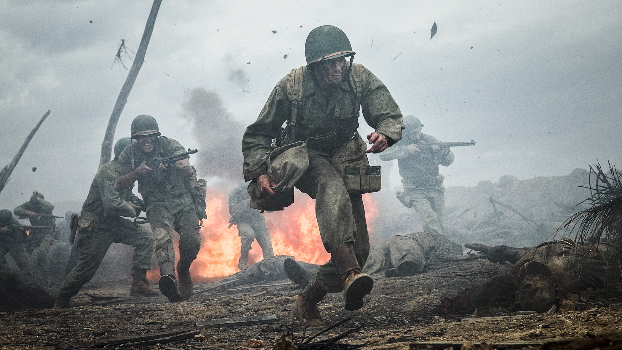 Dramatic scene of soldiers in helmets and military uniforms running and holding weapons amidst smoke and fire during battle.