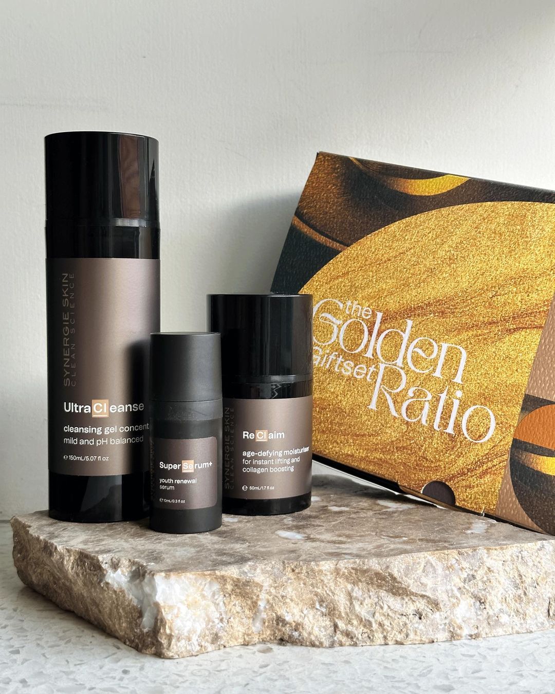 Synergie Skin cleanser, serum, and moisturizer product line displayed on a stone surface with the golden ratio gift set.