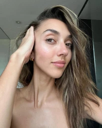 Close-up portrait of a woman touching her highlighted hair with a neutral expression