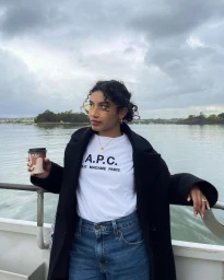 Woman in black coat and white t-shirt holding coffee cup on a ferry with water background