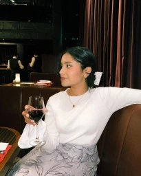 Woman in white sweater holding a wine glass while seated in a restaurant booth by Sharon De Silva