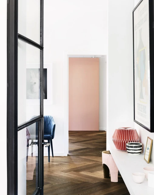 Interior view of modern hallway with herringbone wood floors, white walls, black-framed doorway, decor items, and a peach-colored accent wall.