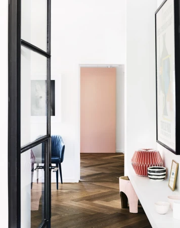 Interior view of modern hallway with herringbone wood floors, white walls, black-framed doorway, decor items, and a peach-colored accent wall.