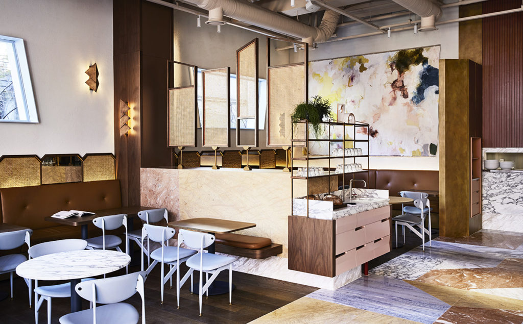 Interior view of a stylish cafe with eclectic furniture, marble surfaces, modern chairs, warm lighting, and a diverse flooring pattern.