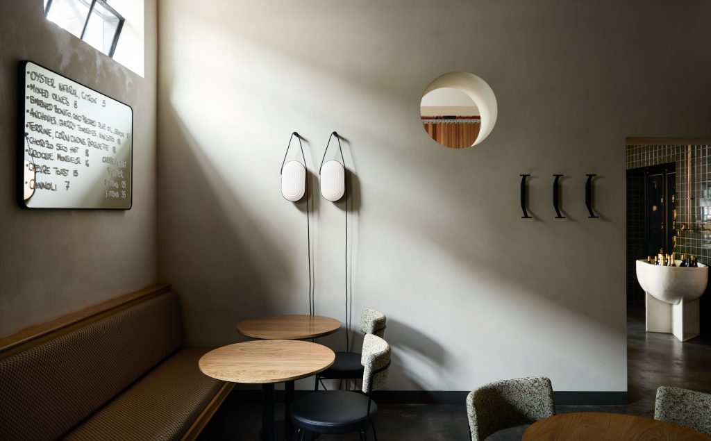 Interior view of a restaurant showcasing a banquette, tables, chairs, wall lamps, menu board, and architectural details, evoking a modern and stylish atmosphere.