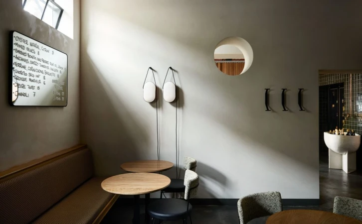 Interior view of a restaurant showcasing a banquette, tables, chairs, wall lamps, menu board, and architectural details, evoking a modern and stylish atmosphere.
