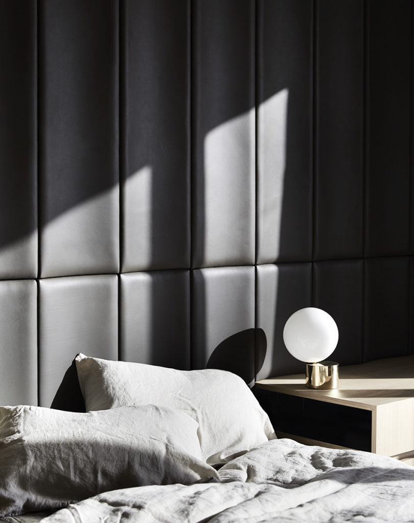 Bedroom interior featuring a bed with white pillows and gray comforter, a white spherical lamp on a wooden nightstand, and a dark gray headboard.