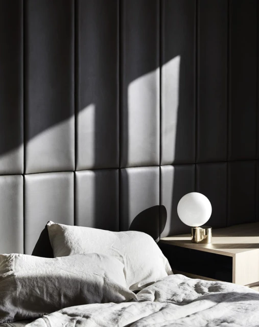 Bedroom interior featuring a bed with white pillows and gray comforter, a white spherical lamp on a wooden nightstand, and a dark gray headboard.