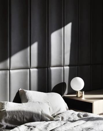 Bedroom interior featuring a bed with white pillows and gray comforter, a white spherical lamp on a wooden nightstand, and a dark gray headboard.