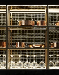 Illuminated kitchen shelving displaying polished copper cookware on top and wine glasses hanging below