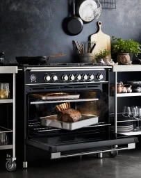 A black range cooker with its oven door open revealing a roasting tin containing a large cut of meat inside.