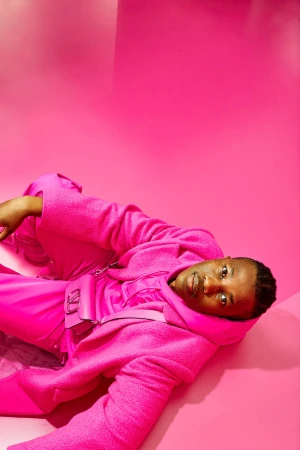 Black man wearing vibrant pink jacket and trousers lying against a matching pink studio backdrop