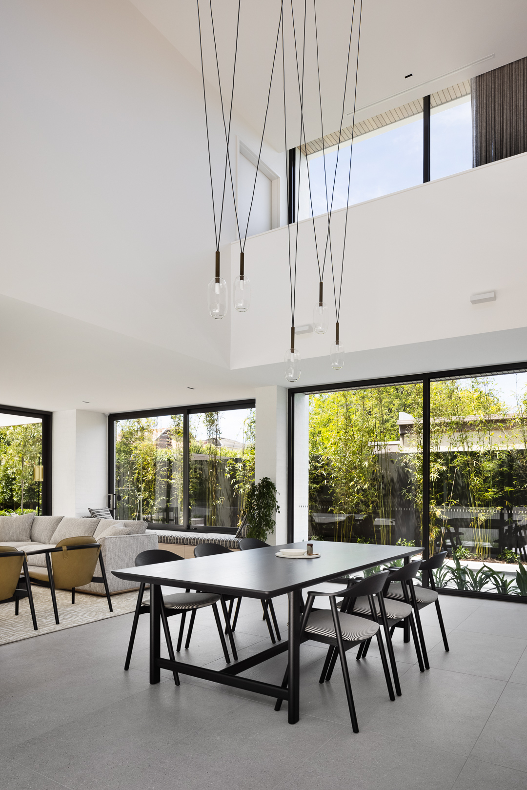 Dining room interior featuring a black dining table with six chairs, pendant lights, and large windows overlooking an outdoor space.