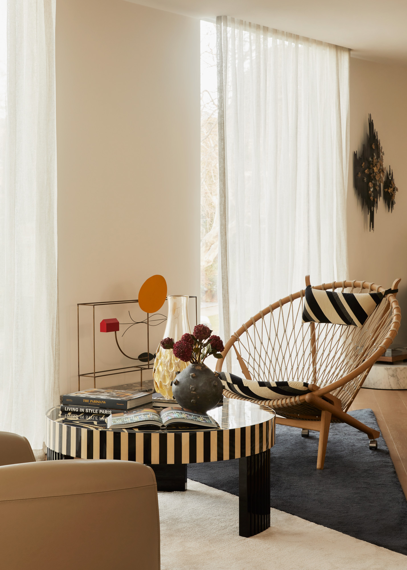 Interior view of a living room with a round striped coffee table, vase with flowers, decorative objects, and a stylish woven chair.