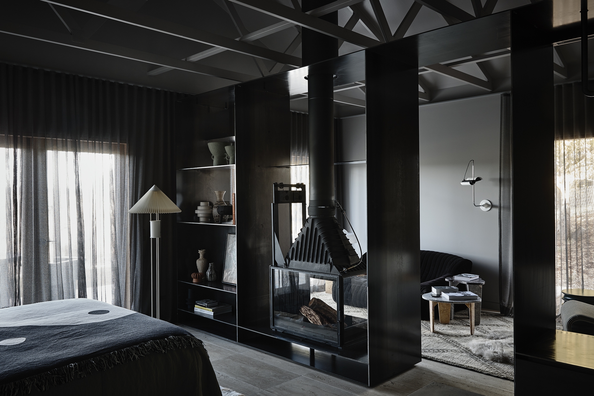 Monochromatic interior with a black fireplace, dark walls, and sheer curtains creating a modern and minimalist bedroom and living space.