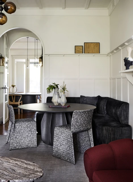 Interior view of a stylish dining room with a round table, upholstered chairs, and a built-in corner bench under framed artwork.